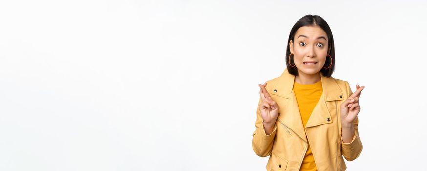 Portrait of excited asian woman looks hopeful, wishing, praying or begging, waiting for news, standing over white background, smiling enthusiastic.