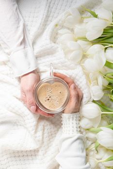 hands of two women holding a heart-shaped cup with cappuccino on two sides, female friendship, flat lay with white tulips, mother's day, valentine's day,