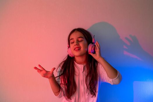 Adorable Little girl in pink headphones dancing to music in neon pink blue light