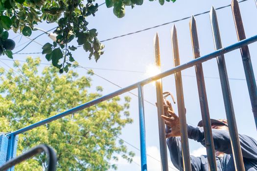 Closeup of the hands of a blue collar worker from Latin America welding a metal fence outdoors.