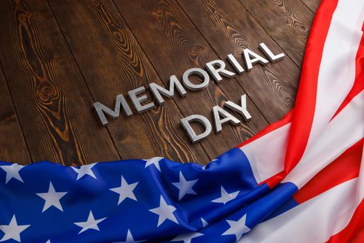 the words memorial day laid with silver metal letters on wooden board surface with crumpled usa flag.