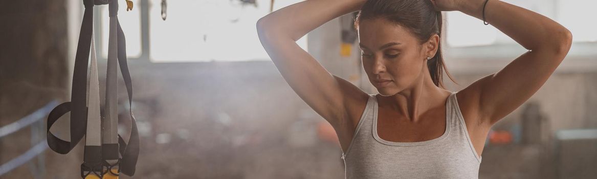 Sporty woman in sportswear adjusting her hair when preparing for workout with fitness straps at gym club