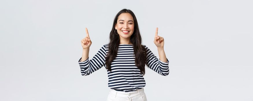 Lifestyle, beauty and fashion, people emotions concept. Cheerful good-looking female model pointing fingers up to shop promotion banner, smiling camera, recommend click link to online store.