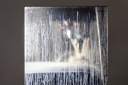 rectangular window of abstract vertical milling machine covered with white coolant liquid drops and smudges, closeup with selective focus