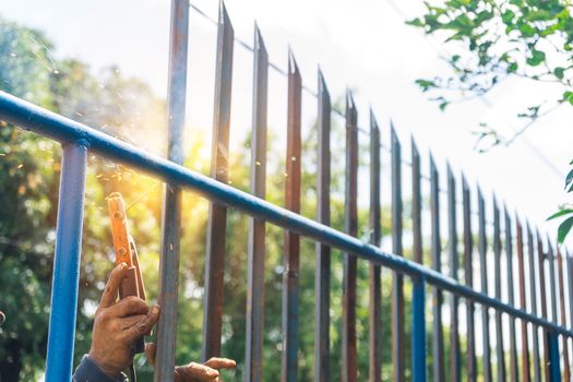 Closeup of the hands of a blue collar worker from Latin America unsafe welding a metal fence outdoors.