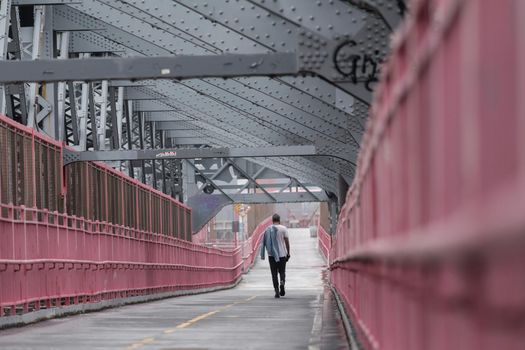 Solo casual man walking the cycling lane on Williamsburg Bridge, Brooklyn, New York City, USA on overcast day.