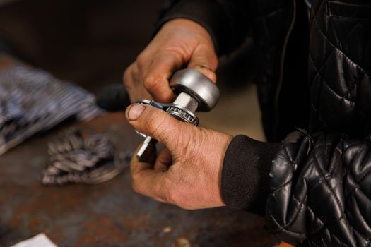 dirty hands of caucasian car technician holding silver adjustable oil filter wrench, close-up with selective focus