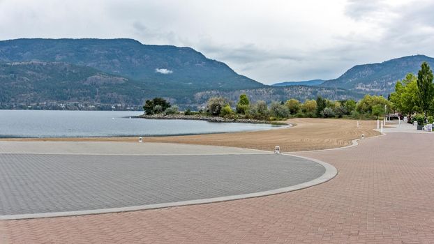 Paved walkway along the waterfront of Okanagan lake. Landscaped beach on overcast rainy day in Kelowna, British Columbia