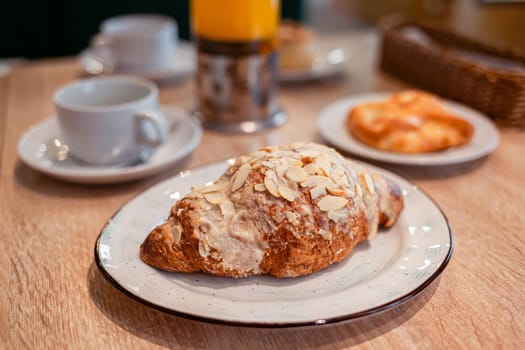 A fresh large croissant on a beautiful plate in a cafe or restaurant. Close-up of a croissant and cream sprinkled with nuts. Sweet and delicious dessert for coffee time.