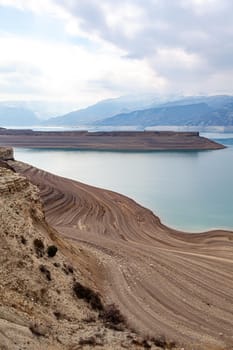 A beautiful reservoir in the mountains. Low water level, drought and beautiful patterns are visible along the banks. A red pleasure boat is standing by the shore