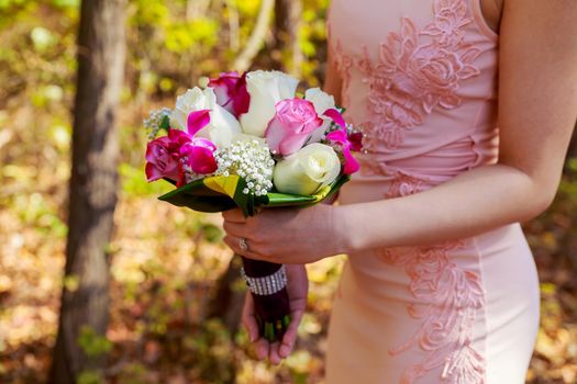 young caucasian woman in pink lace dress holds a bouquet with flowers and pink garden roses in her hands