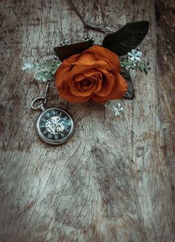 Orange rose flower and A retro pocket watch on old wooden board background. Copy space, No focus, specifically.