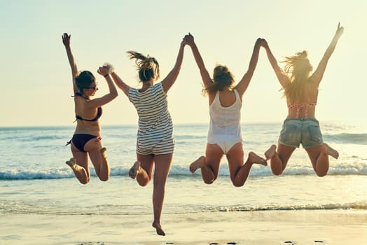 Rearview shot of female best friends jumping in the air at the beach.