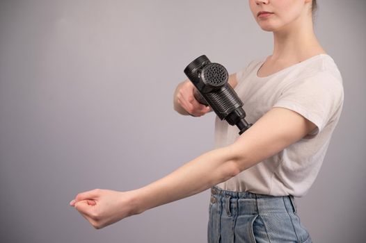 Caucasian woman uses a massager gun for pain in the muscles of the arm