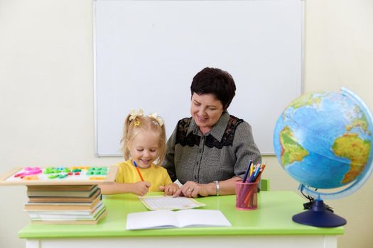 Mature teacher sitting at table having class with a little girl