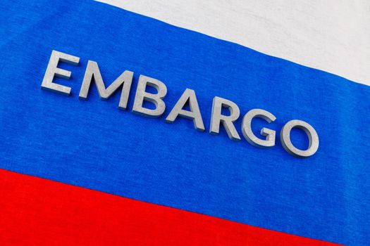 the word embargo laid with silver metal letters on russian tricolor flag in diagonal perspective view