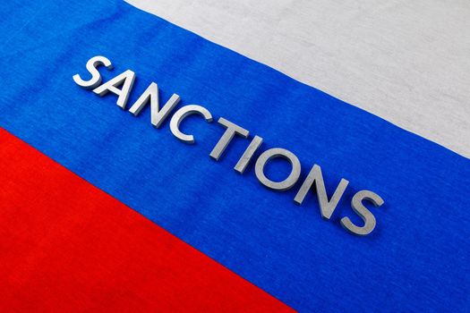 the word sanctions laid with silver metal letters on russian tricolor flag in diagonal linear perspective