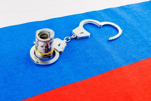 roll of us dollar banknotes in a handcuffs on flat full-frame russian flag, closeup