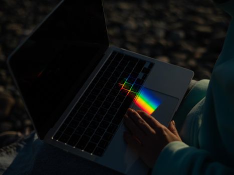 A woman is typing on a laptop. Rainbow light from a prism