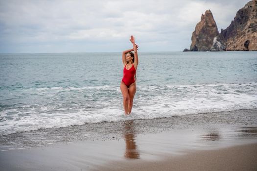 A beautiful and sexy brunette in a red swimsuit on a pebble beach, Running along the shore in the foam of the waves.