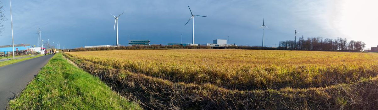 panorama of a field with windmills and industry in the background on a sunny day