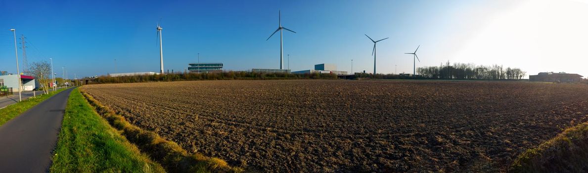 panorama of a field with windmills and industry in the background on a sunny day