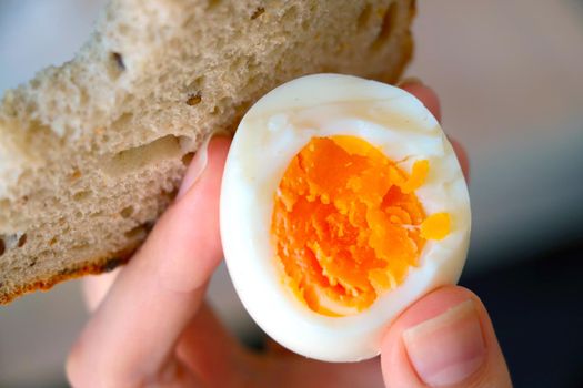 The girl holds a boiled egg and bread in her hand, a quick and healthy snack