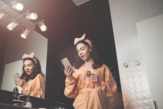 Portrait view of beautiful young woman getting ready in home bathroom. mirror face reflection. Bathroom decorated with a black tiles