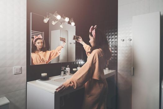 Portrait view of beautiful young woman making selfie in home bathroom. mirror face reflection. Social networks, communication.