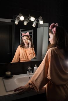 Portrait view of beautiful young woman getting ready in home bathroom. mirror face reflection. Bathroom decorated with a black tiles