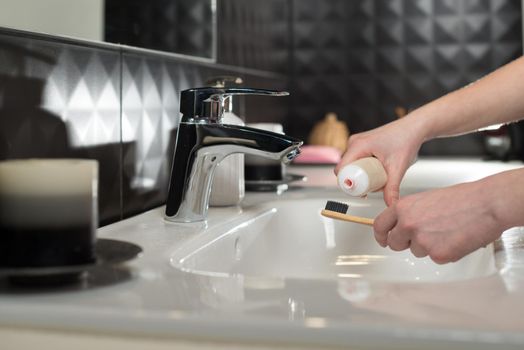 Closeup female hand is holding ecological bamboo brush with whitening toothpaste. woman is preparing going to clean teeth. Tool for oral care. Personal hygiene product concept.