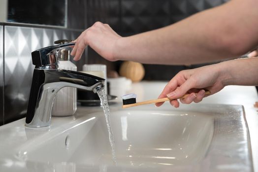 Closeup female hand is holding ecological bamboo brush with whitening toothpaste. woman is preparing going to clean teeth. Tool for oral care. Personal hygiene product concept.