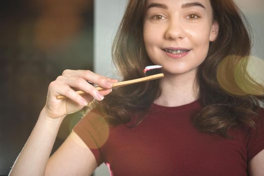 Woman brushing her teeth. Young woman in a burgundy top with bamboo brush. Bathroom with a black tiles