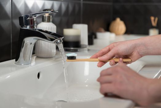 Closeup female hand is holding ecological bamboo brush with whitening toothpaste. woman is preparing going to clean teeth. Tool for oral care. Personal hygiene product concept.