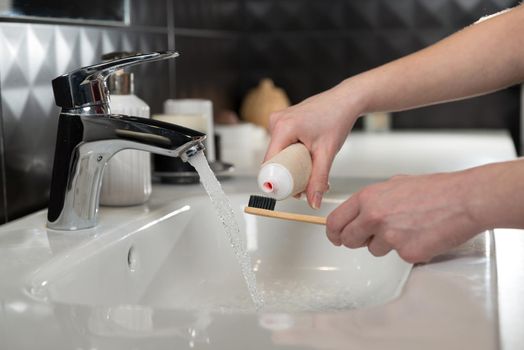 Closeup female hand is holding ecological bamboo brush with whitening toothpaste. woman is preparing going to clean teeth. Tool for oral care. Personal hygiene product concept.