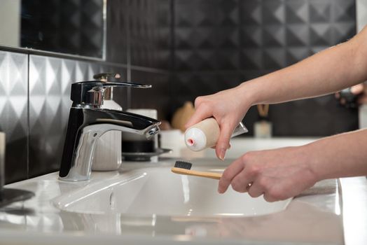 Closeup female hand is holding ecological bamboo brush with whitening toothpaste. woman is preparing going to clean teeth. Tool for oral care. Personal hygiene product concept.