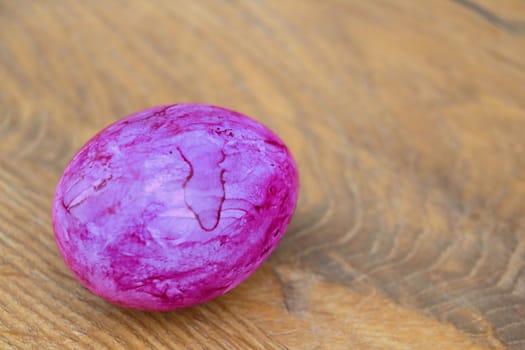 Purple colored egg on a wooden table. Preparing for Easter