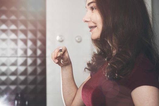 Woman brushing her teeth. Young woman in a burgundy top with bamboo brush. Bathroom with a black tiles