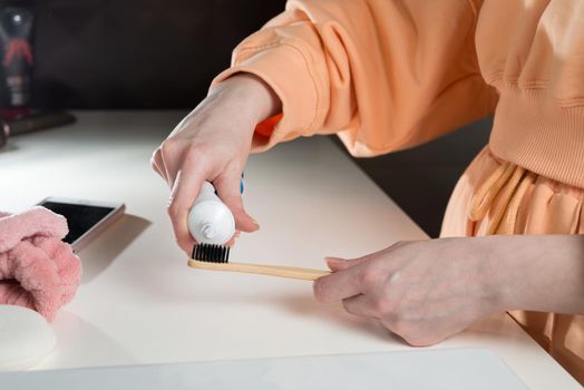 Closeup female hand is holding ecological bamboo brush with whitening toothpaste. woman is preparing going to clean teeth. Tool for oral care. Personal hygiene product concept.