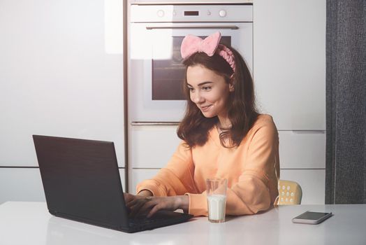 Young woman in a kitchen catching up and having fun while studying on a laptop computer. Distance Learning. work at a distance
