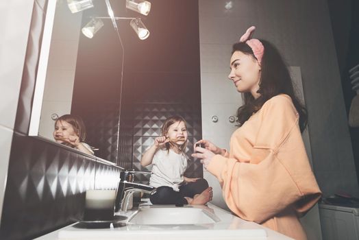 happy family and health. mother and daughter baby girl brushing their teeth together. mom holds a little jar of cream