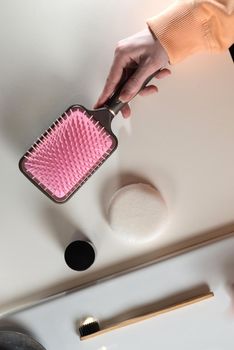 top view of bathroom accessories, toothbrush near hair brush, bow, mobile phone and face sponge on a white surface.