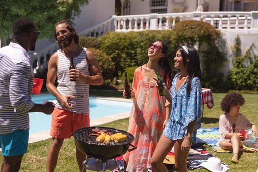 Diverse group of friends having barbecue and talking at a pool party. hanging out, drinking beer and relaxing outdoors in summer.