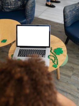 Mixed race woman celebrating st patrick's day on laptop video call with copy space on screen. fun during celebration of the irish patron saint's day.