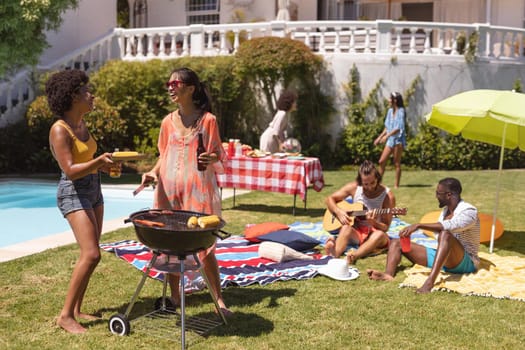 Diverse group of friends having barbecue and talking at a pool party. Hanging out and relaxing outdoors in summer.