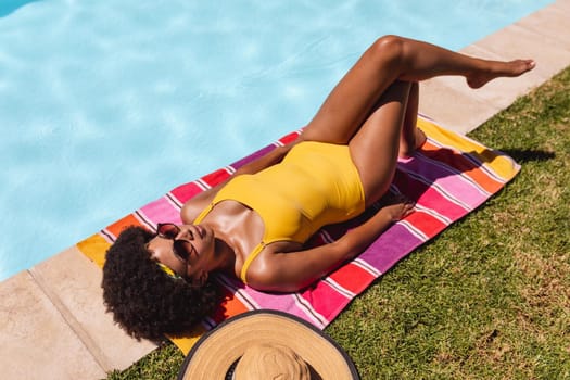 Mixed race woman sunbathing by pool on a sunny day. Hanging out and relaxing outdoors in summer.