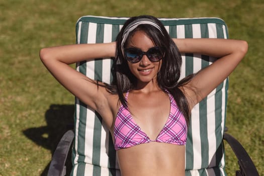 Mixed race woman wearing sunglasses sunbathing on sunbed in garden. Hanging out and relaxing outdoors in summer.