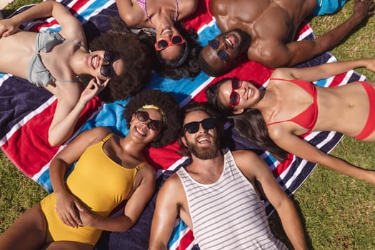 Diverse group of friends sunbathing together on a sunny day smiling. Hanging out and relaxing outdoors in summer.