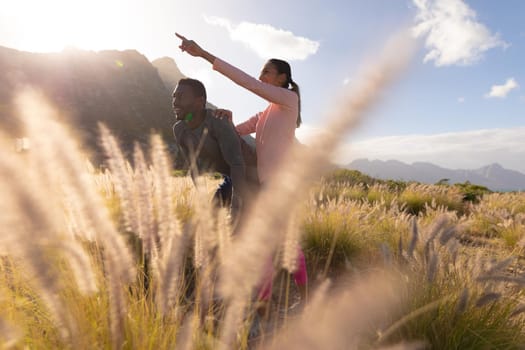 Fit african american couple in sportswear resting leaning on knees in tall grass. woman is pointing finger. healthy lifestyle, exercising in nature.