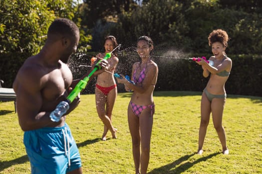 Diverse group of friends having fun playing with water guns at a pool party. hanging out and relaxing outdoors in summer.